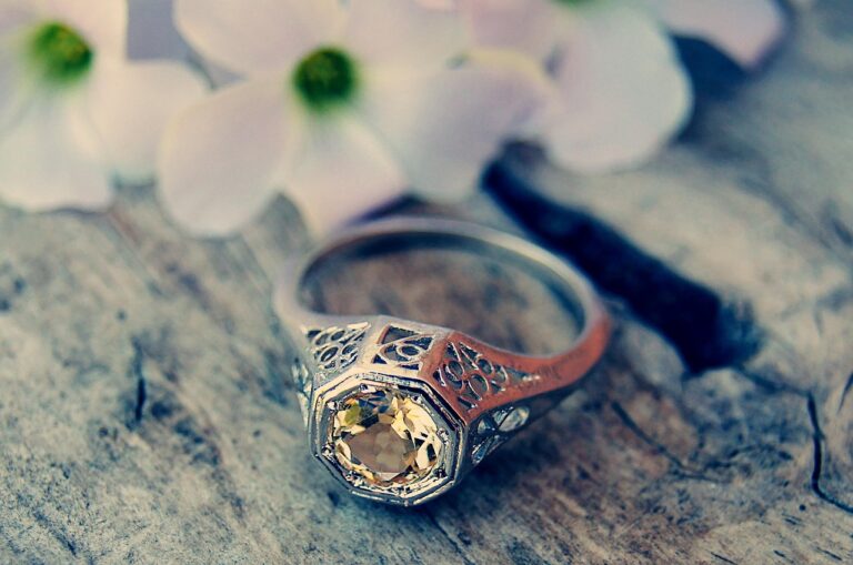 Old fashioned engagement ring with yellow gemstone on wooden surface and white flowers
