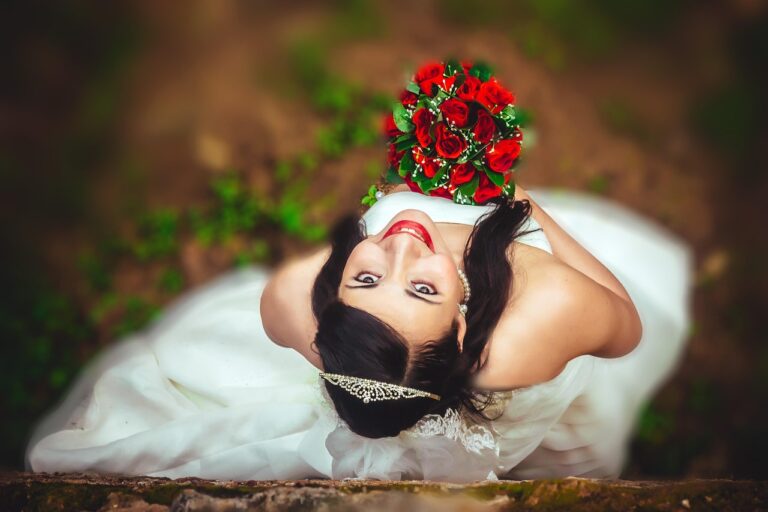 Simple elegant wedding decor: bride in white dress with tiara holding red rose bouquet outdoors