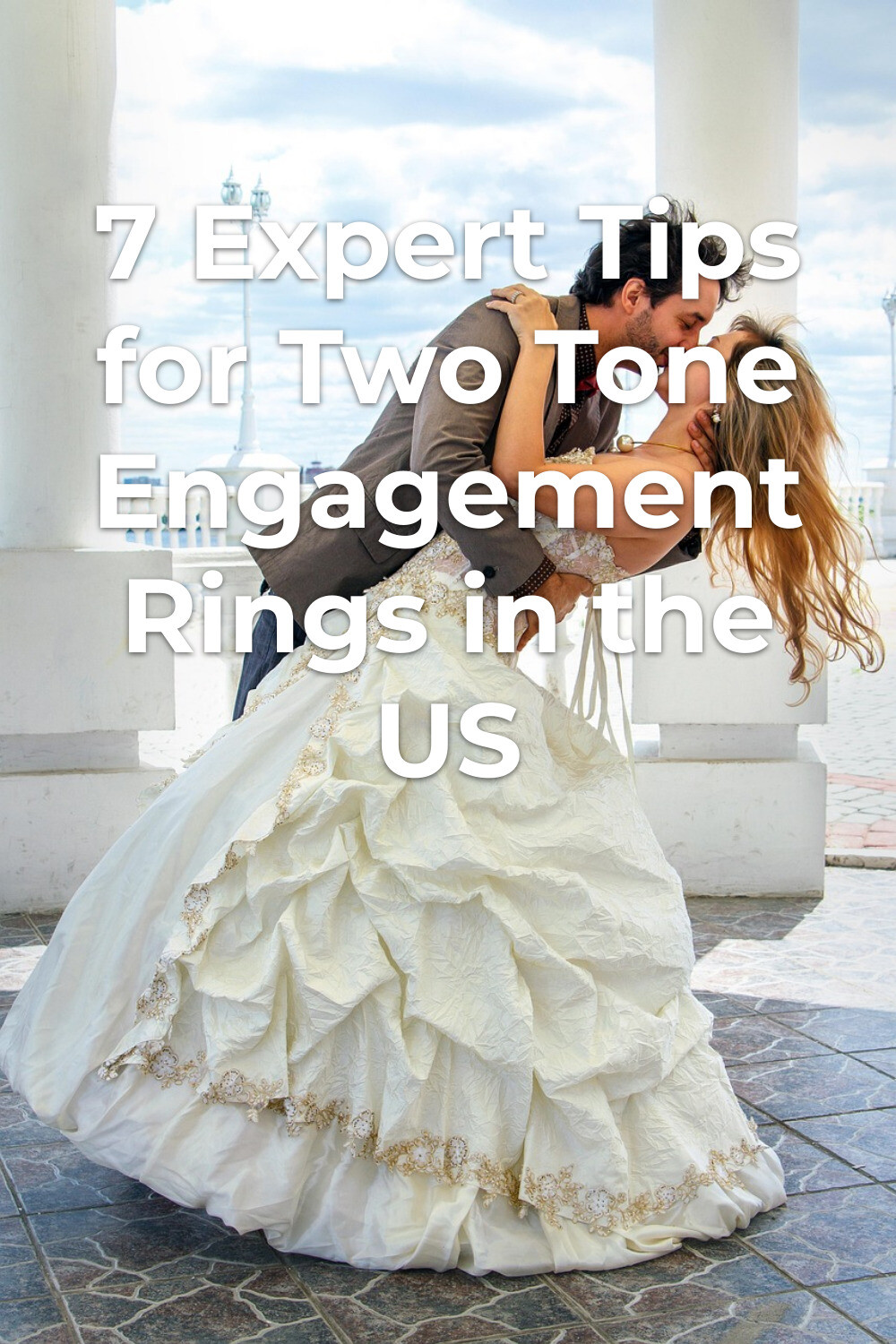 Two tone engagement rings shine as a groom kisses his bride in a romantic outdoor dip between white columns.