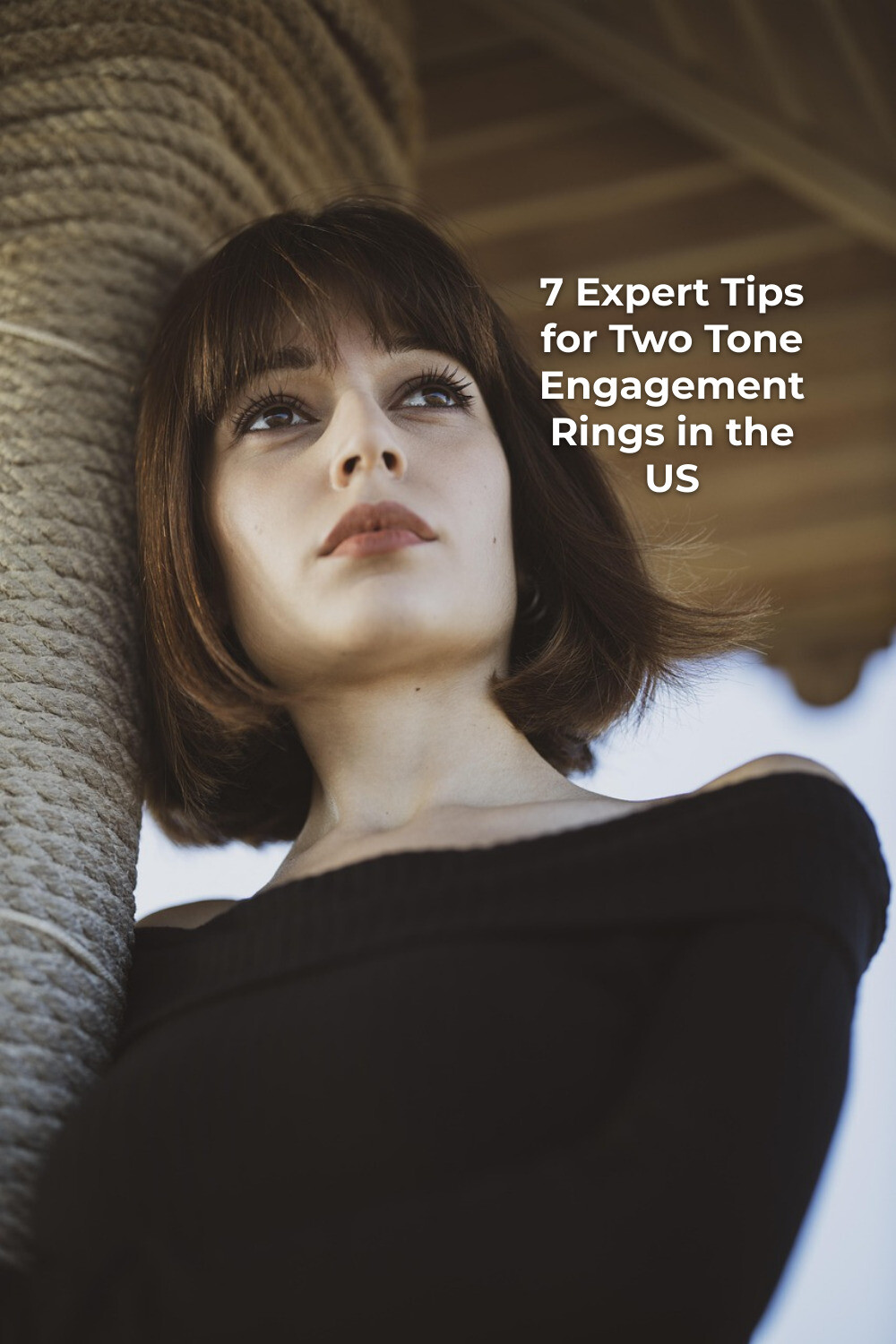 Woman in black top leaning on stone column under wooden roof, looking up; two tone engagement rings inspiration