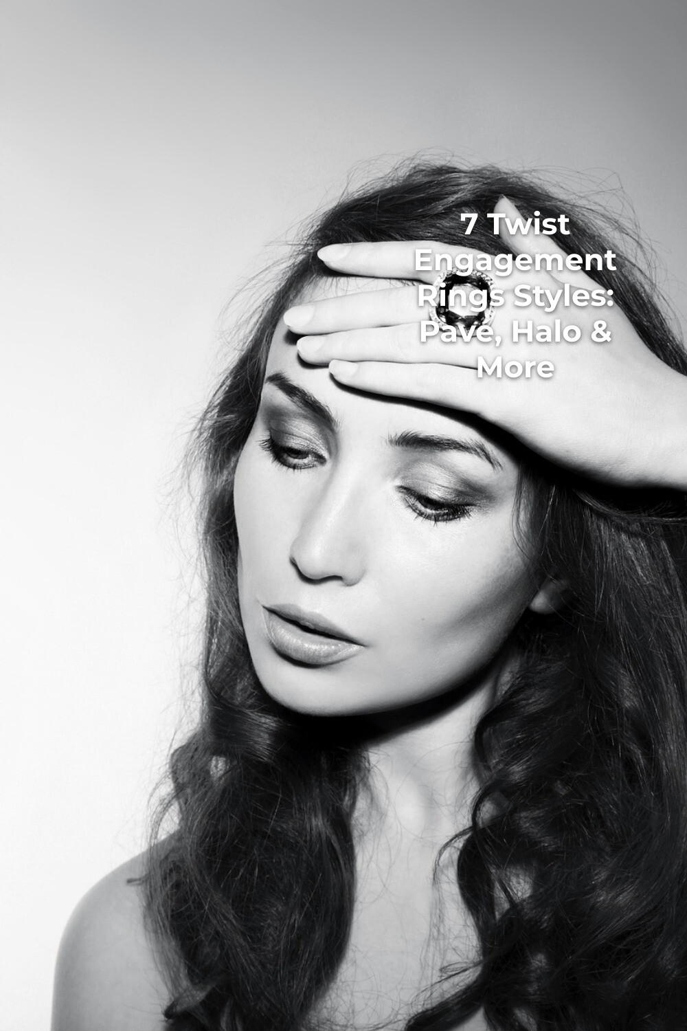 Woman with long wavy hair showing a large twist engagement ring against a plain background