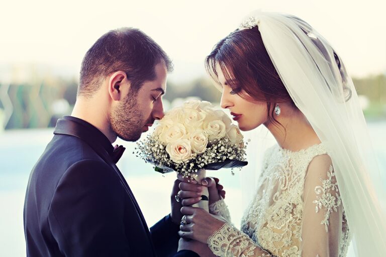 Entrance wedding decor with bride in lace veil and groom in dark suit holding white rose bouquet outdoors