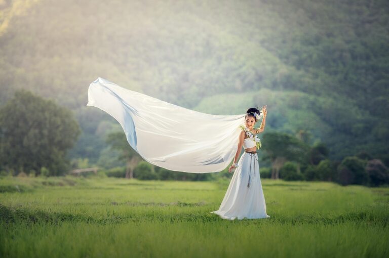 Greenery wedding decor with bride in white dress holding long white fabric in a green field with hills