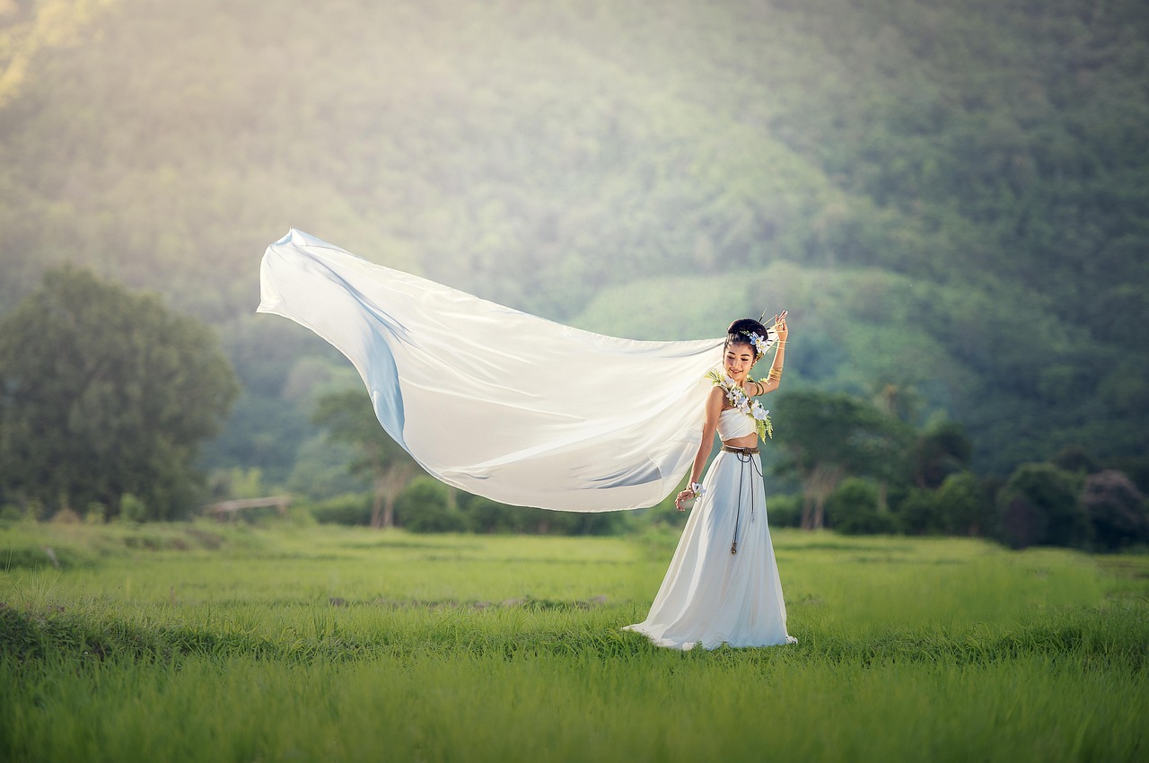Greenery wedding decor with bride in white dress holding long white fabric in a green field with hills
