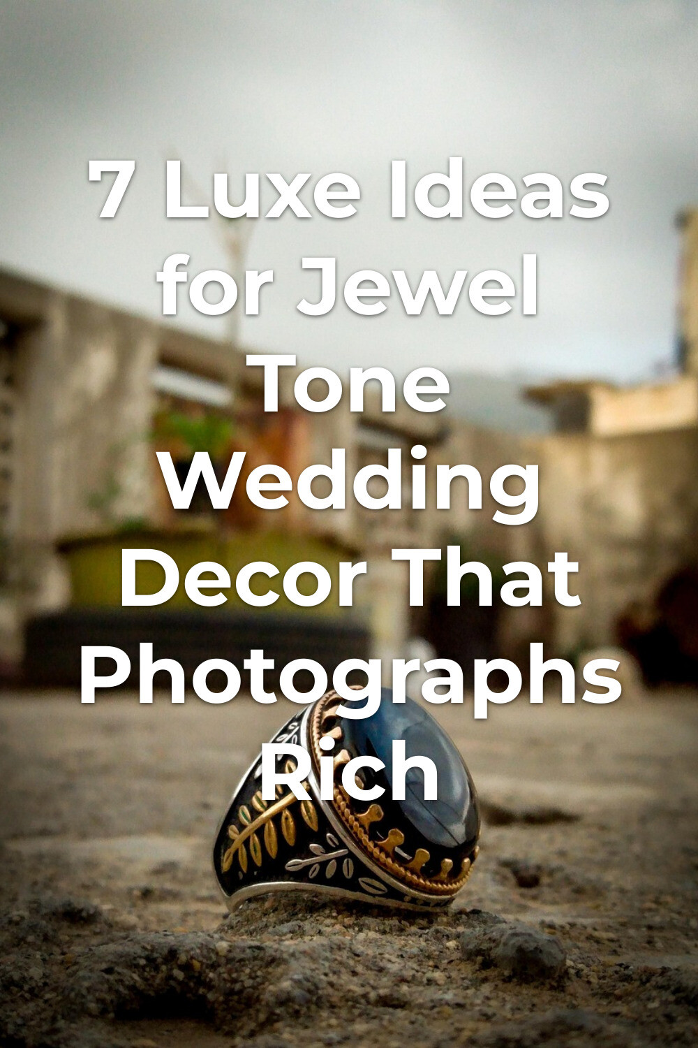 Jewel Tone Wedding Decor Ring Detail Jewel tone wedding decor detail with a dark oval stone ring on rough ground, blurred buildings and cloudy sky