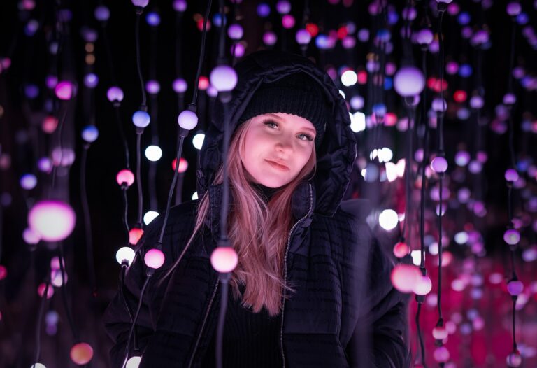 Woman in black coat under pink and purple string lights for romantic garden wedding decor