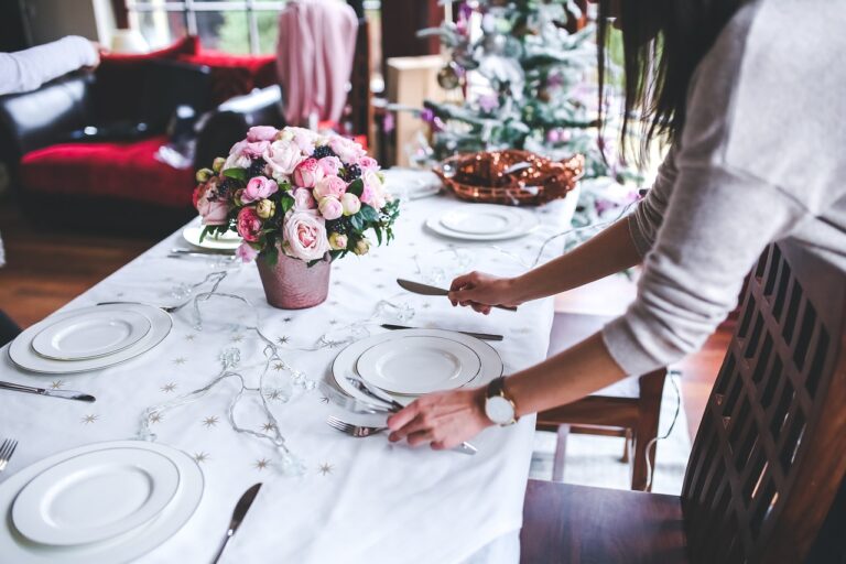 Small wedding decor table setting with white plates, cutlery, and flowers beside a decorated living room tree