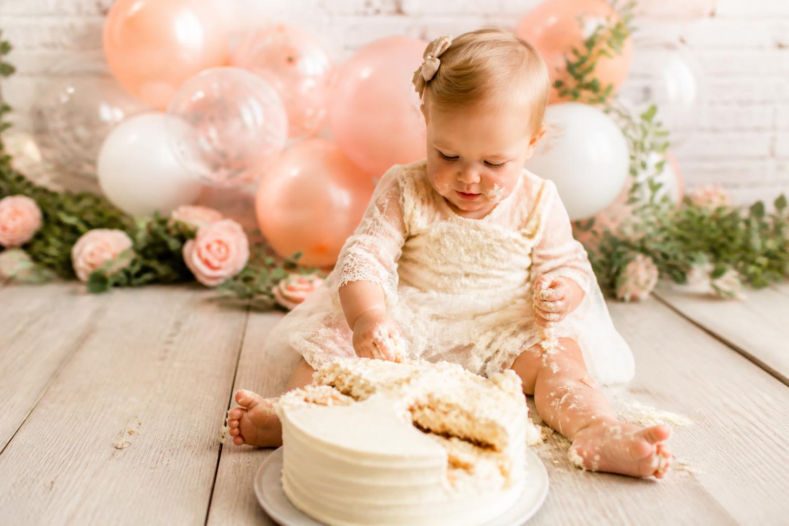 Cake poses photo ideas with baby smiling behind birthday cake in a pastel first birthday portrait