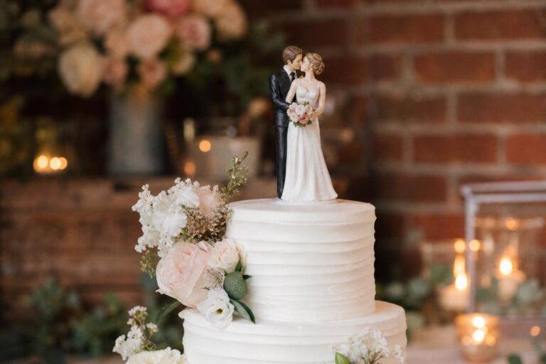 Elegant wedding cake toppers on a white tiered cake at a romantic reception table