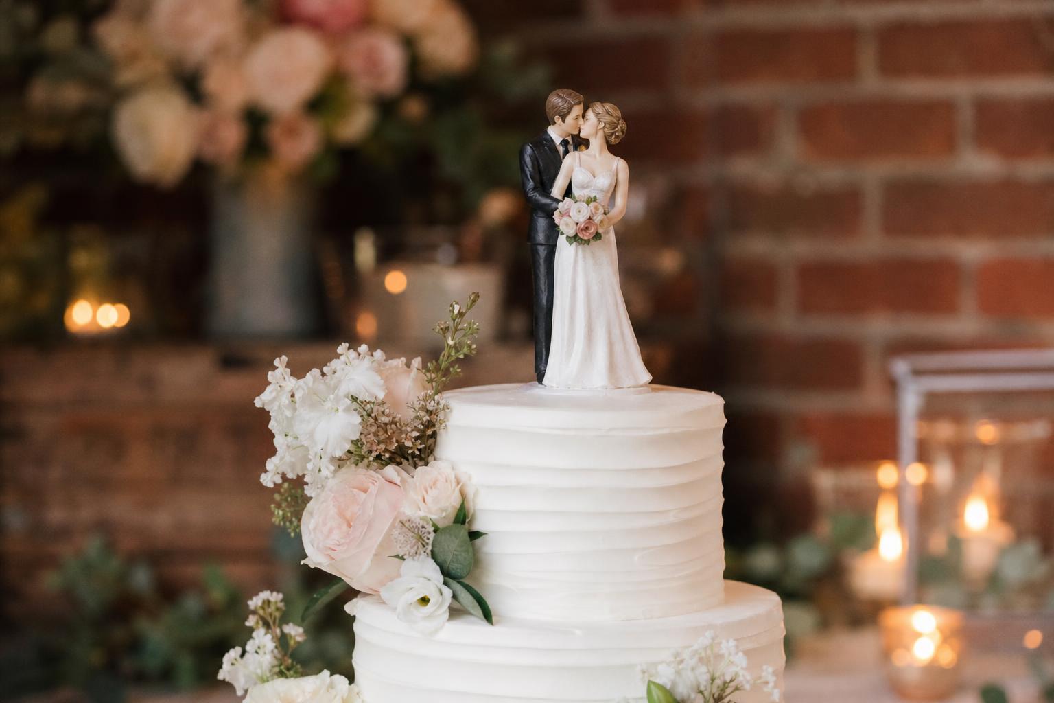 Elegant wedding cake toppers on a white tiered cake at a romantic reception table