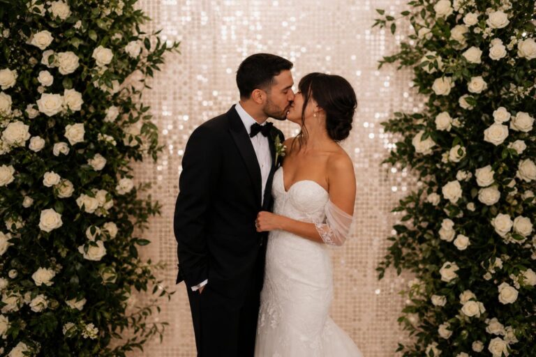 Romantic photo booth couple pictures of newlyweds kissing under a floral wedding backdrop with soft reception lighting