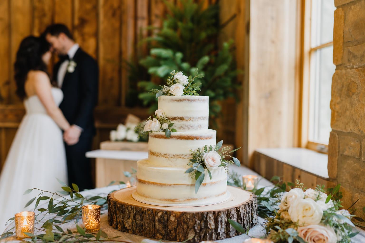 Rustic wedding cake with textured buttercream, olive garland, and fresh flowers on a wooden stand at a candlelit reception