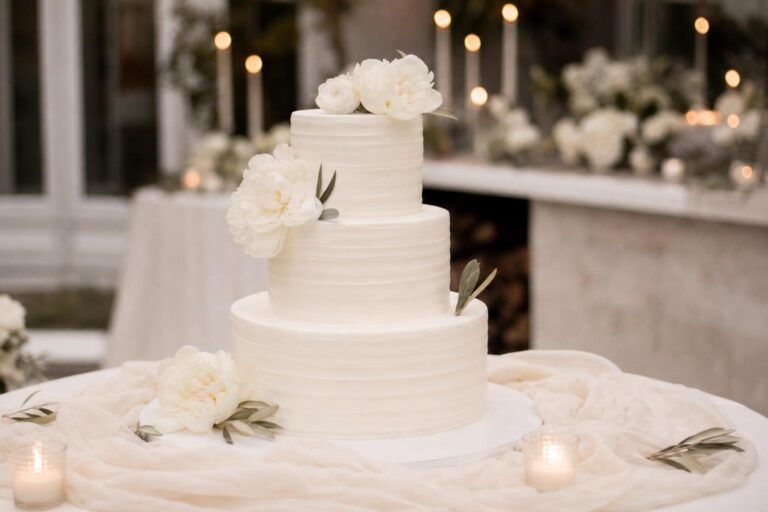 Wedding cake simple elegant with smooth white buttercream tiers and a minimal blush rose accent on a clean cake stand