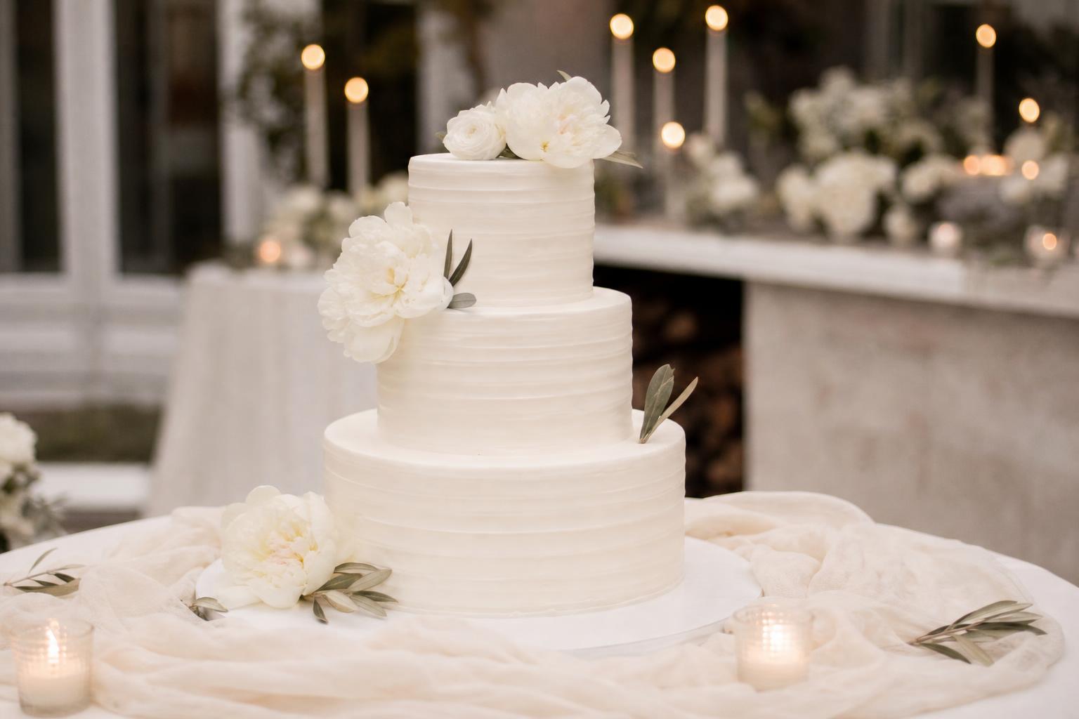 Wedding cake simple elegant with smooth white buttercream tiers and a minimal blush rose accent on a clean cake stand