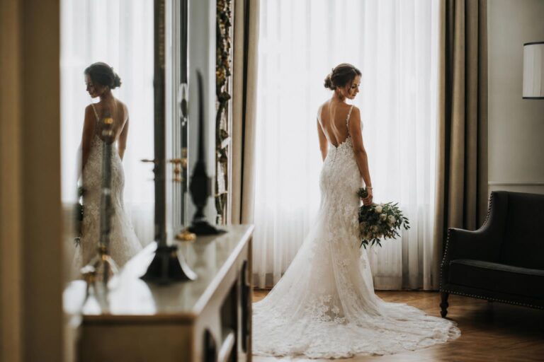 Wedding dress photo ideas with a bridal gown hanging by a bright window in an elegant getting-ready suite