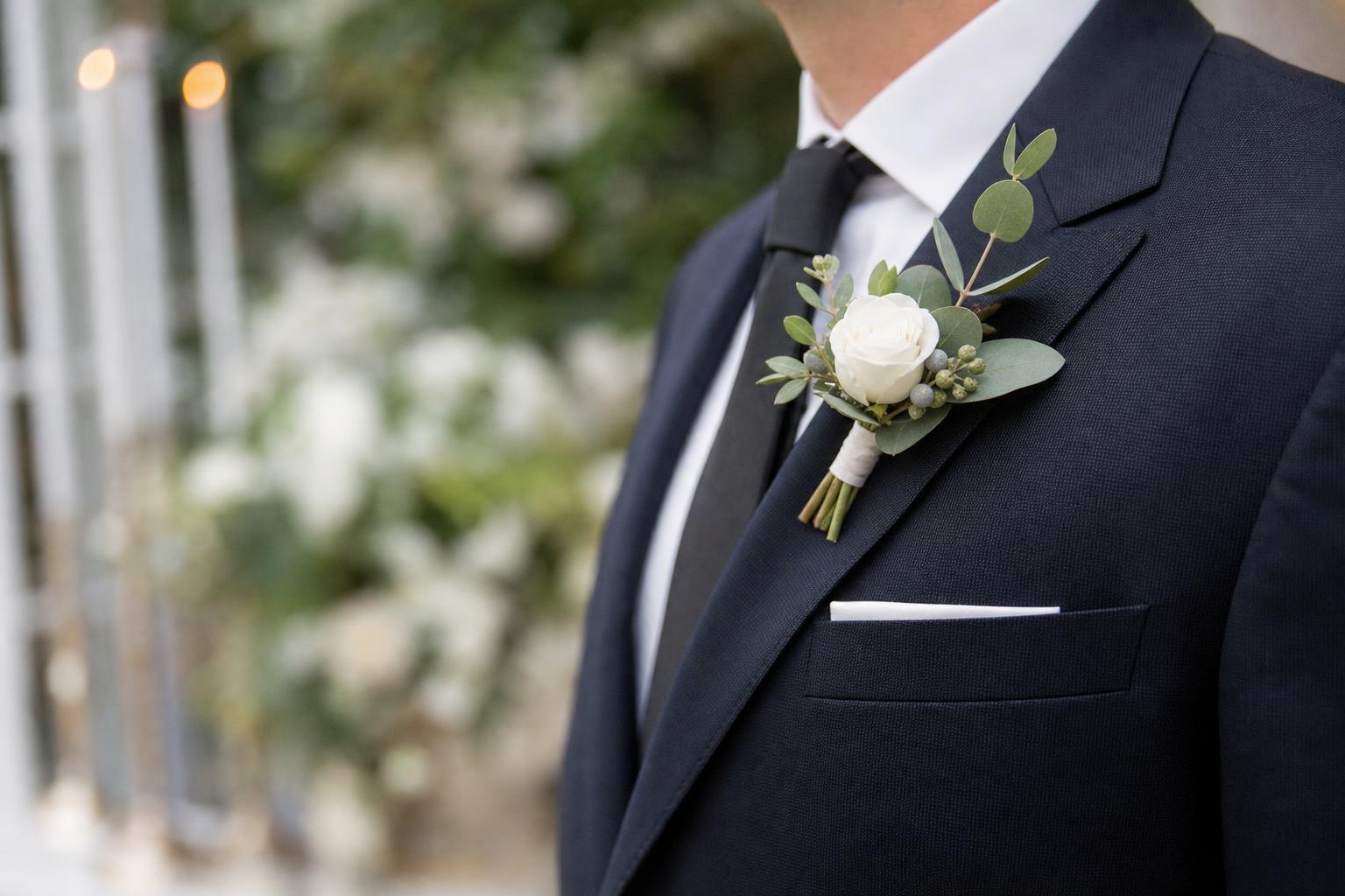 Elegant boutonnieres wedding styling on a groom’s navy suit lapel with white rose and soft greenery