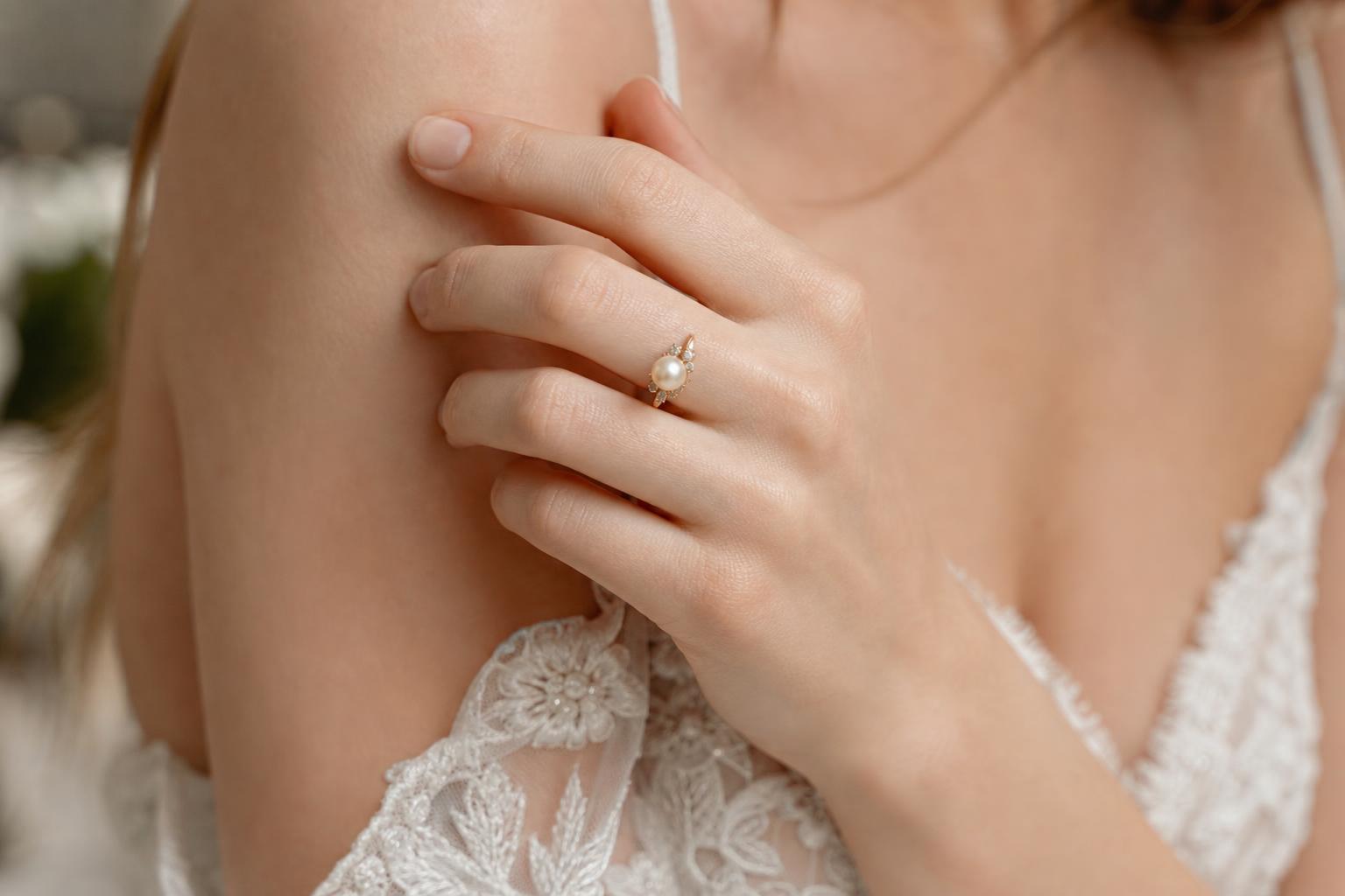 Pearl wedding ring in warm gold with soft luster and delicate diamond accents, photographed on a bride’s hand